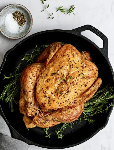 Whole roast Sommerlad Heritage chicken in metal roasting pan, golden and crisp, showcasing natural marbling and rich colour.