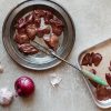 Fresh Sommerlad heritage chicken livers arranged on a stainless steel platter and baking tray, with onion and garlic in the background.