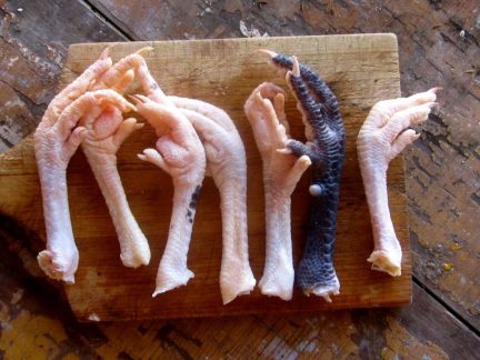 Variety of chicken feet in different colours displayed on a wooden board