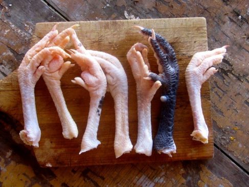 Variety of chicken feet in different colours displayed on a wooden board