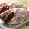 Two meaty chicken frames side-by-side on a white plastic bread board, garnished with fresh sage and lemon.