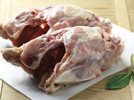Two meaty chicken frames side-by-side on a white plastic bread board, garnished with fresh sage and lemon.