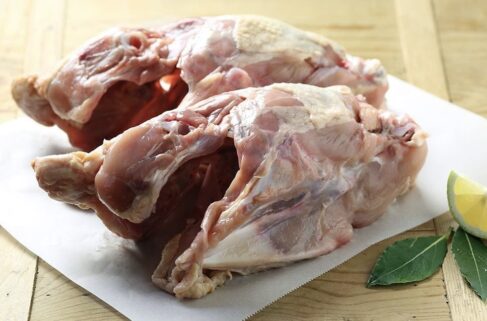 Two meaty chicken frames side-by-side on a white plastic bread board, garnished with fresh sage and lemon.