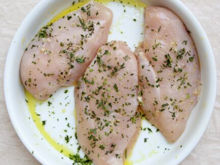 Raw seasoned Sommerlad chicken breasts garnished with parsley and olive oil on a white plate
