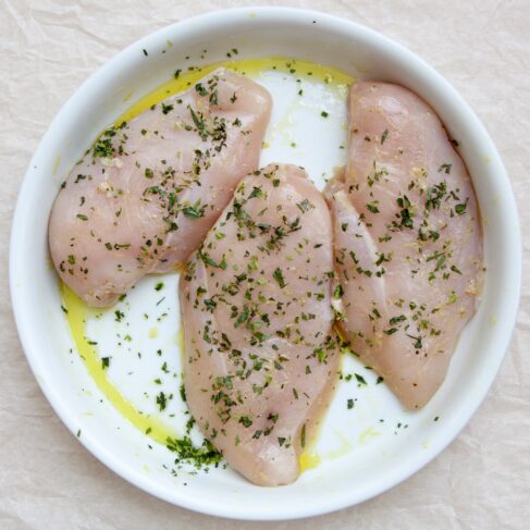 Raw seasoned Sommerlad chicken breasts garnished with parsley and olive oil on a white plate