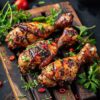 Three grilled chicken drumsticks topped with fresh herbs and chilli on a wooden board.