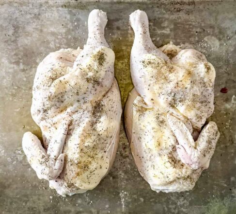Seasoned raw Sommerlad heritage chicken halves on a flat surface, ready to cook.
