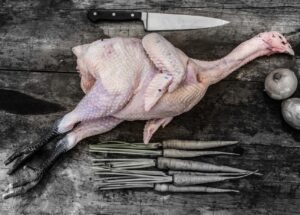 Whole Sommerlad heritage chicken with head and feet on, displayed raw and unseasoned on a wooden board.