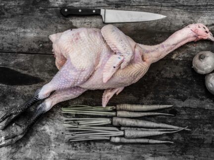 Whole Sommerlad heritage chicken with head and feet on, displayed raw and unseasoned on a wooden board.