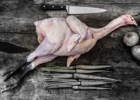 Whole Sommerlad heritage chicken with head and feet on, displayed raw and unseasoned on a wooden board.
