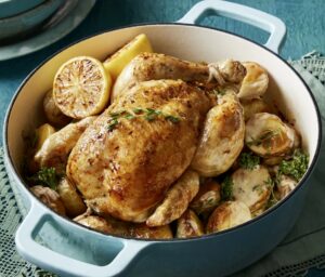Heritage chicken roasting in a pot with golden potatoes and lemon wedges