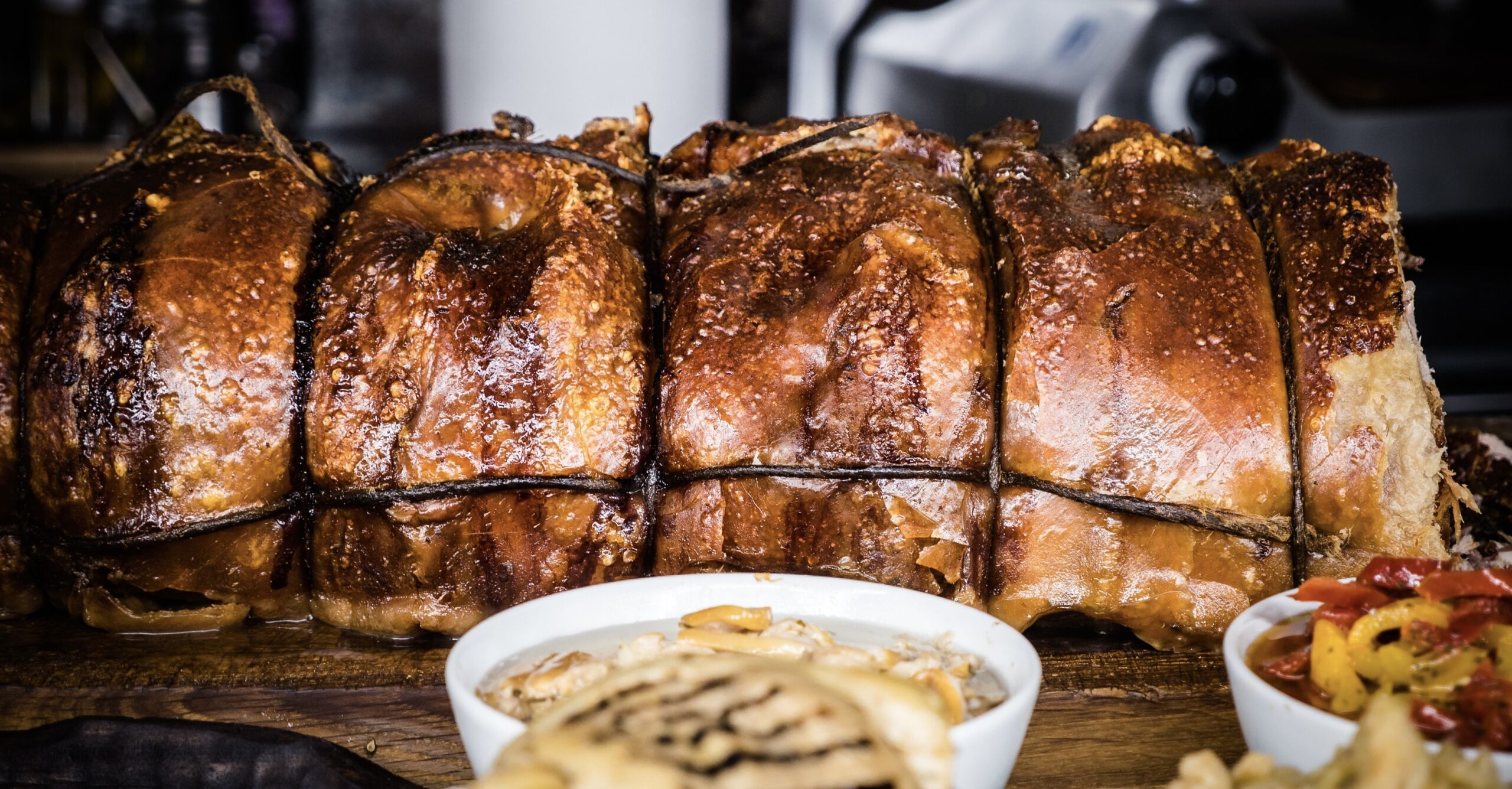 Slow roasted Wuuluman pork porchetta sliced to reveal tender pork and crisp golden crackling Whole roasted Wuuluman pork porchetta fresh from the oven, with crisp golden skin, made from regenerative pastured heritage pork.